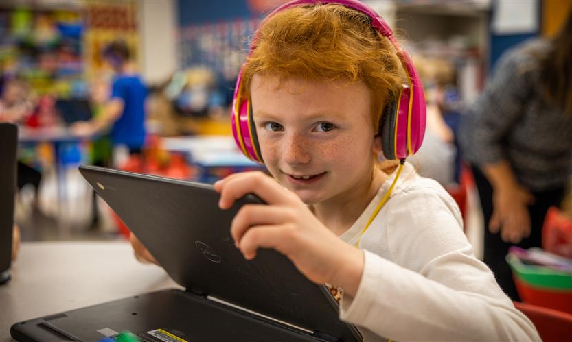 A girl with red hair and wearing headphones smiles